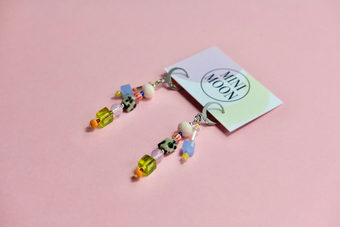 Colorful beaded earrings on a pink background with a card labeled 'Mini Moon'.