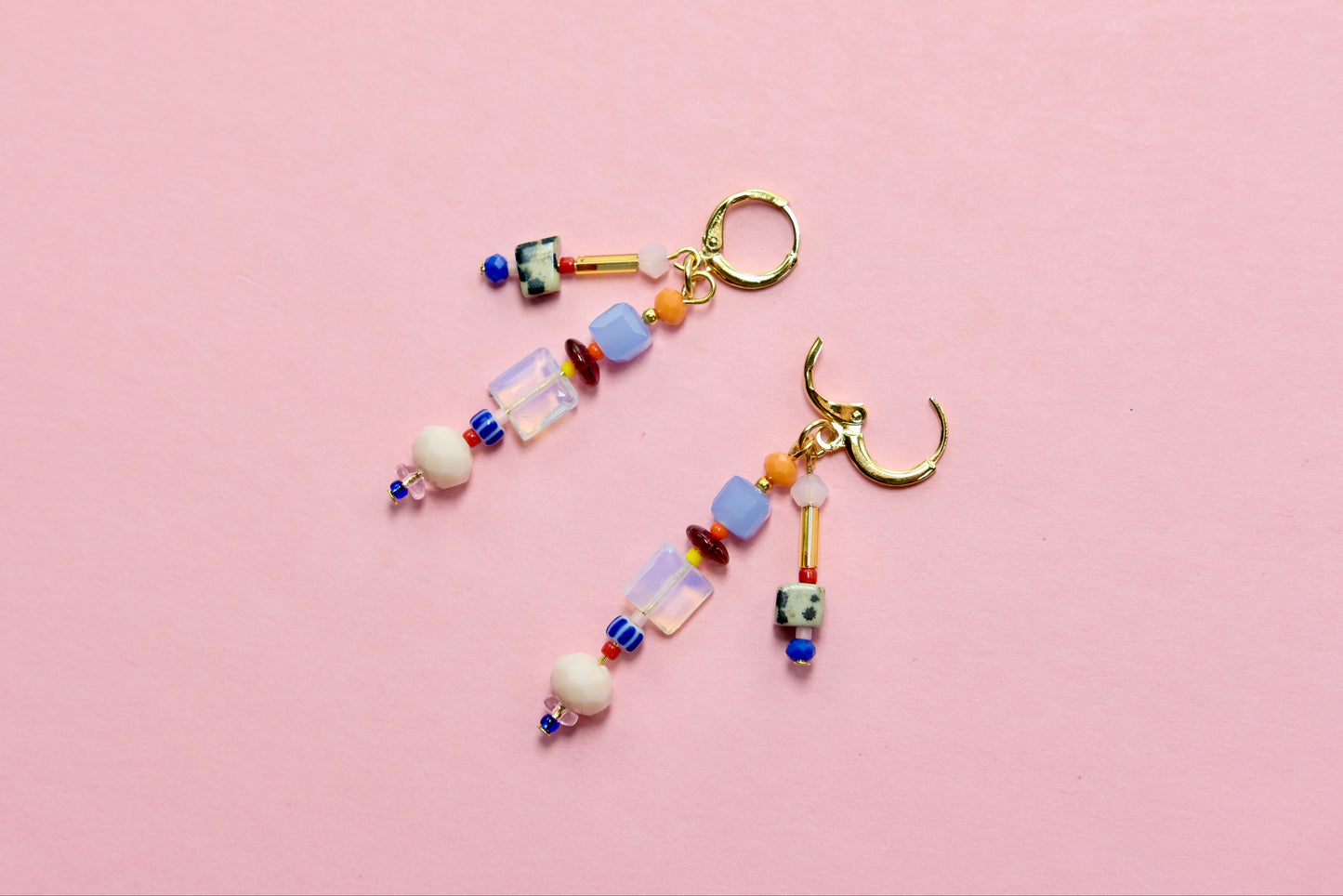 Colorful beaded earrings with charms on a pink background