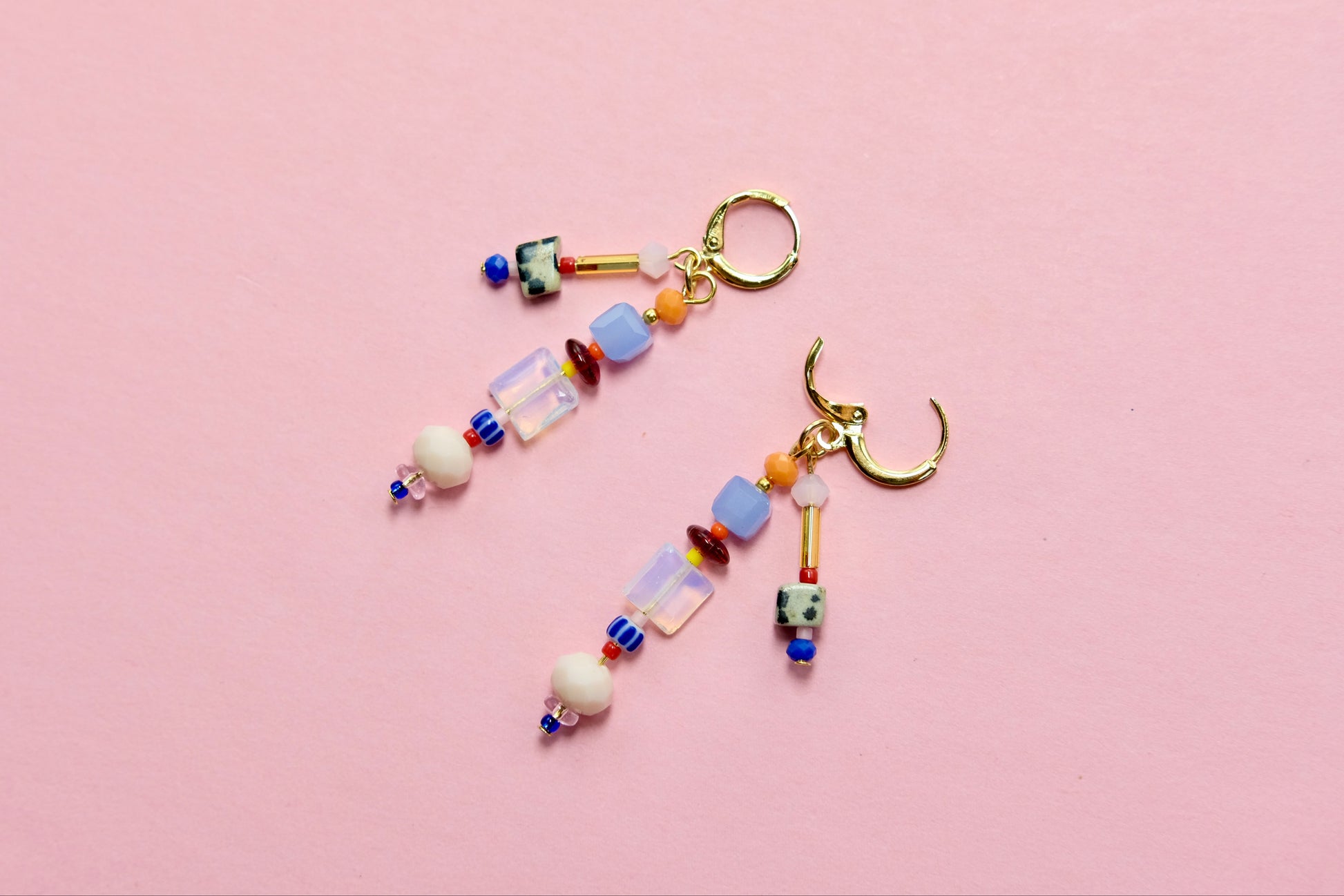 Colorful beaded earrings with charms on a pink background