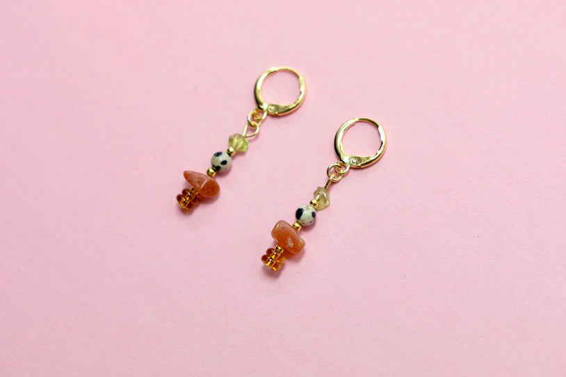 Pair of earrings with earthy beads on a pink background
