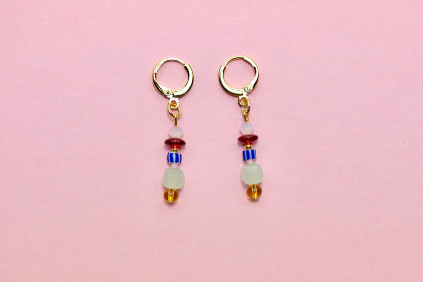 Pair of earrings with colorful beads on a pink background