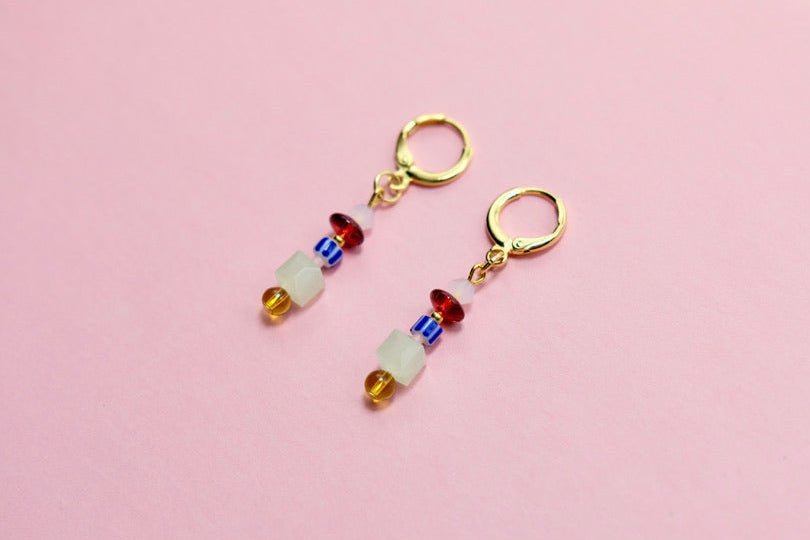 Pair of gold earrings with colorful beads on a pink background