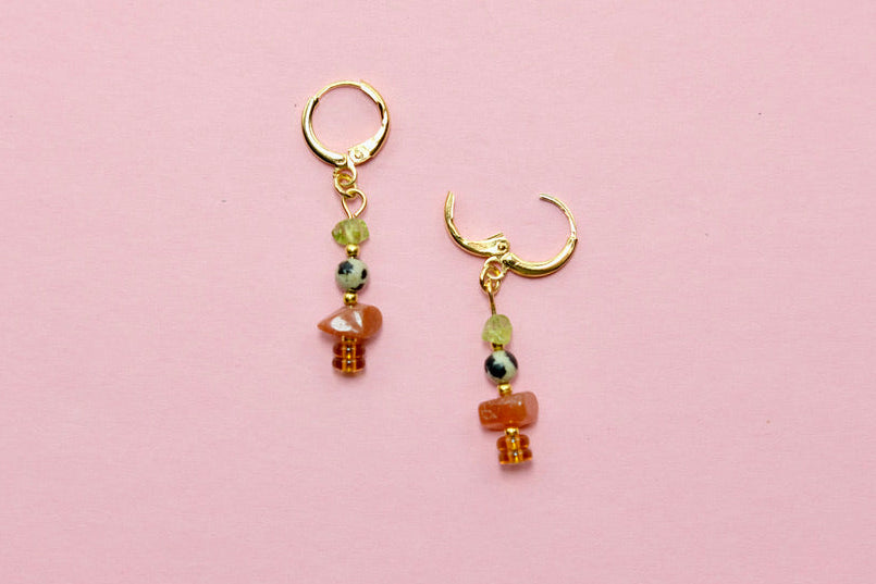 Pair of gemstone earrings with beads on a pink background