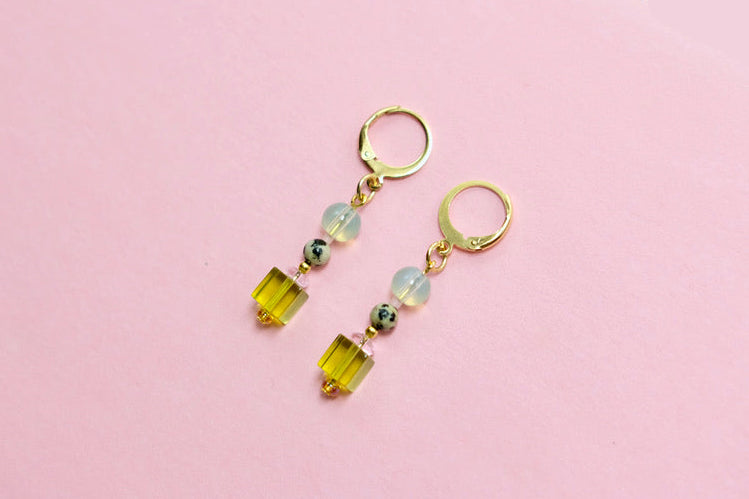 Gold earrings with colorful beads on a pink surface