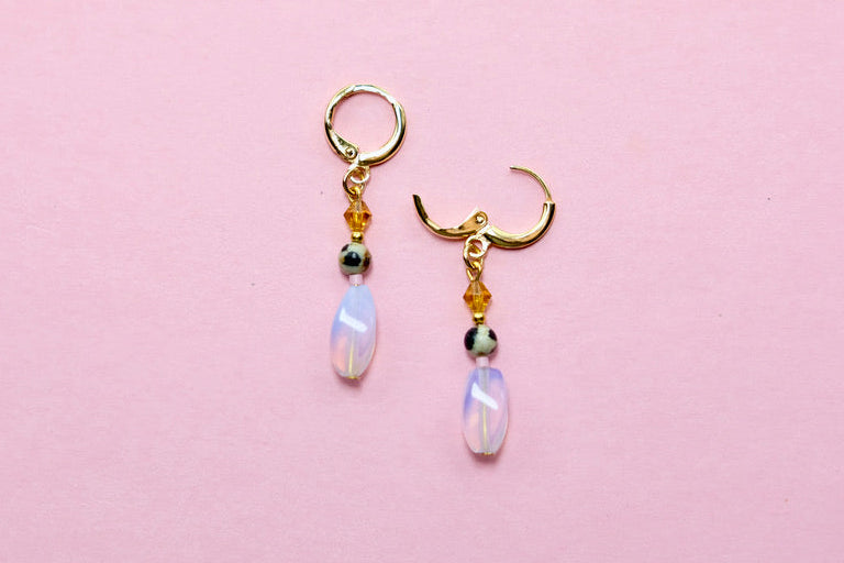 Pair of earrings with rainbow opal drops on a pink background