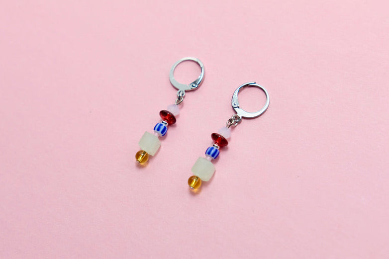 Pair of earrings with colorful beads on a pink background