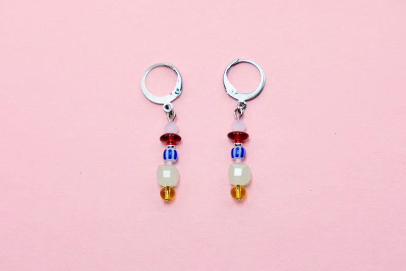 Pair of earrings with colorful beads on a pink background